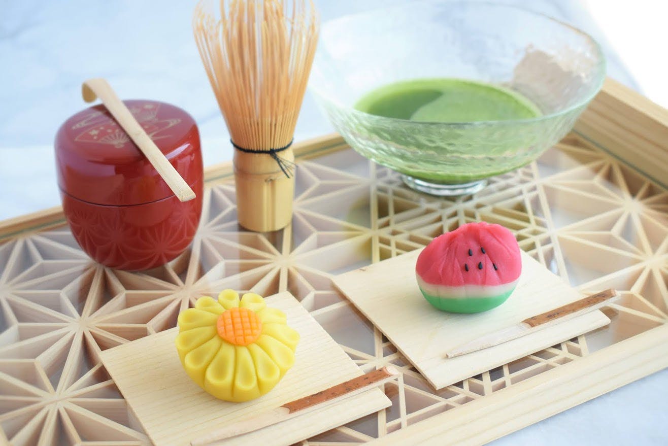 Image of two Japanese sweets shaped like a watermelon and sunflower next to a cup of green tea.
