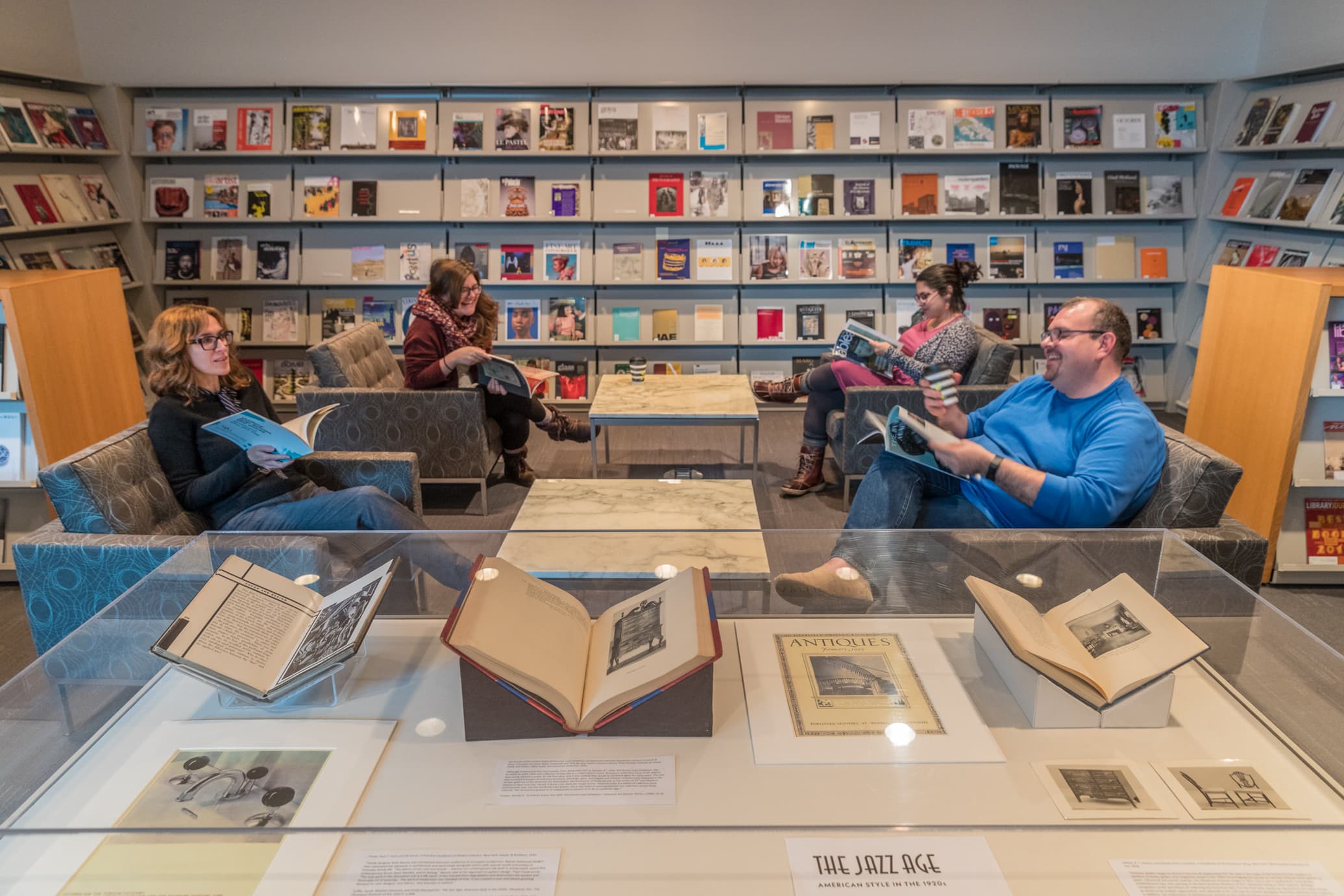 patrons reading and display case in library, with wall-to-wall bookshelves displaying periodicals