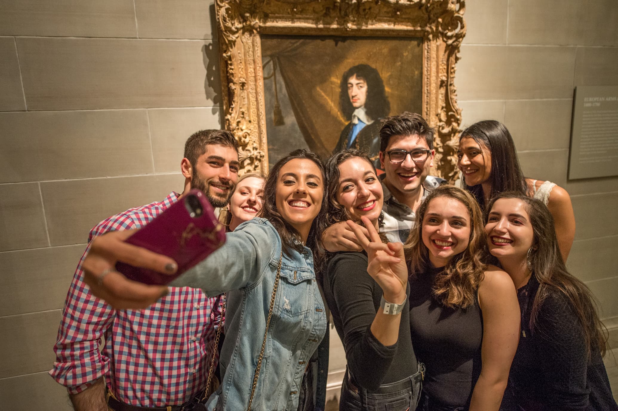 Group of visitors smile and pose for selfie in front of framed painting