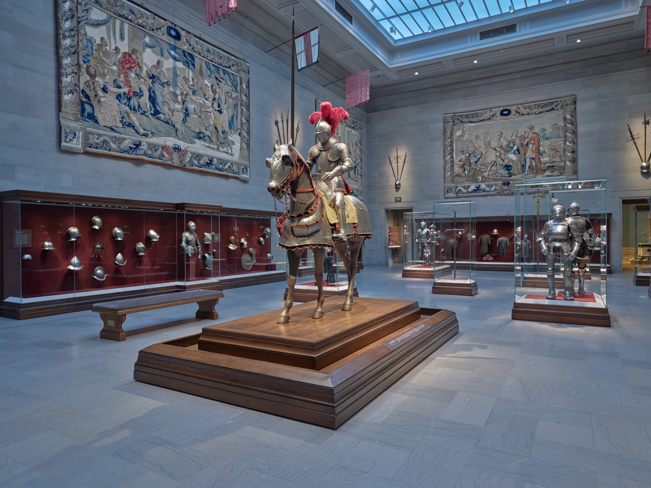 armored figure on horseback in center of large gallery, surrounded by cases of arms and armor