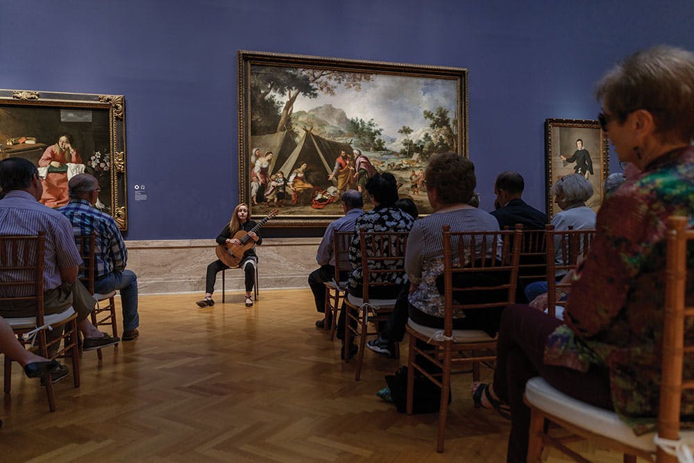 Woman in with guitar preforming for crowd of people in museum