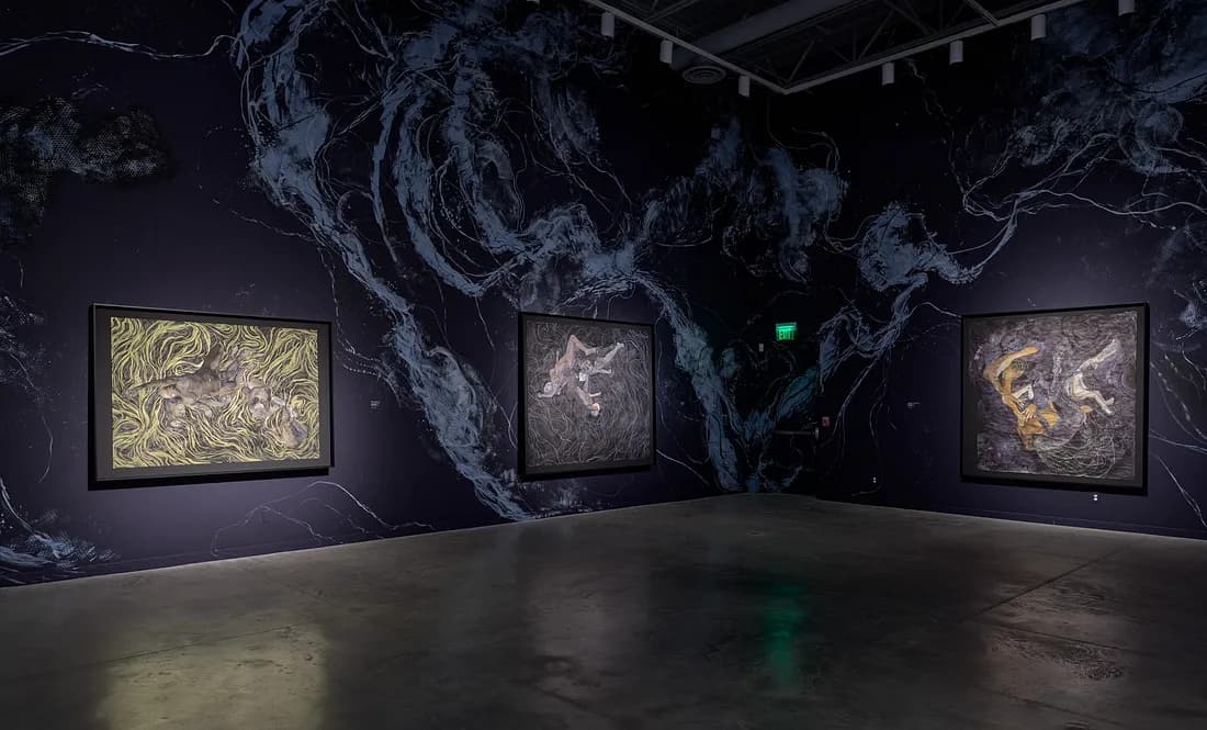 Exhibition with dark blue, marbled wall on which three artworks with curving lines are hung.