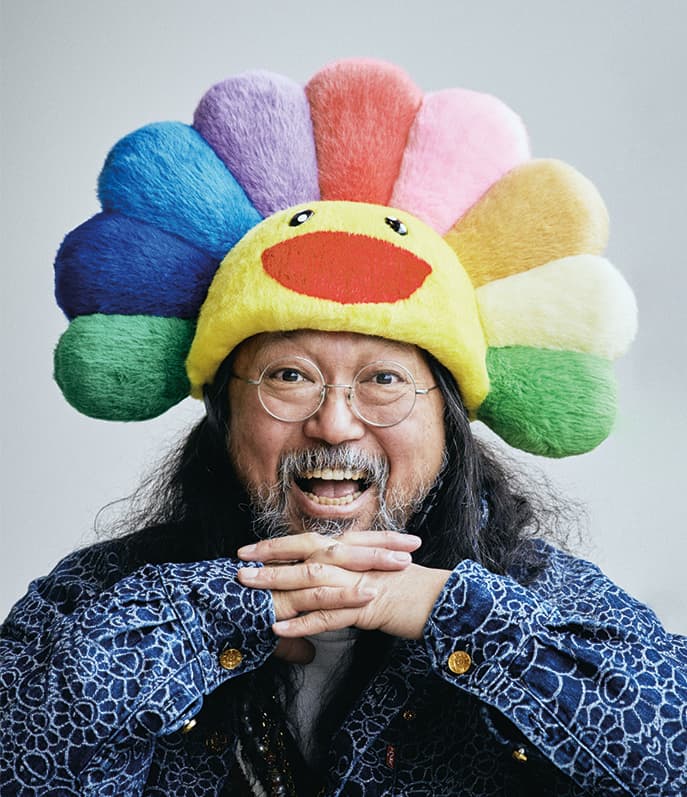 Takashi Murakami smiling and wearing a rainbow flower hat.