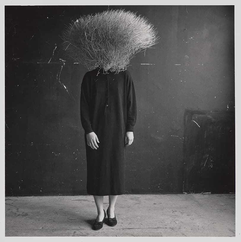 woman in black with plant on head covering face