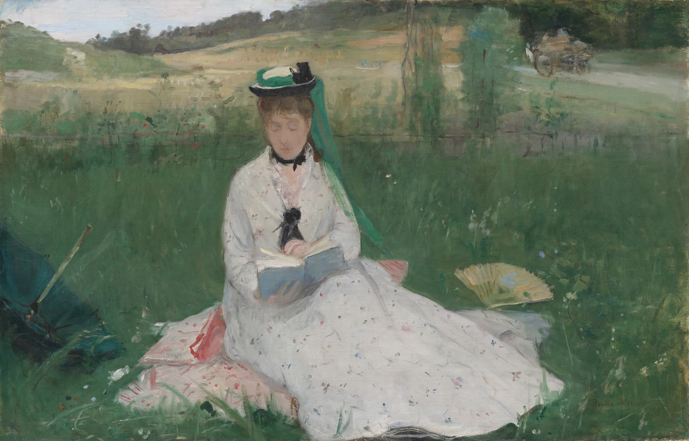 A horizontally oriented oil painting in loose brushstrokes depicts Edma Morisot, a woman with light skin tone in a white dress seated reading a blue book on a pink blanket over grass. The dress, blanket, and grass are all patterned with flecks of paint. The woman's facial features are only hazily suggested under a hat with a green veil hanging down. An open fan lies in the grass to her right and there is light brown grass in the background.