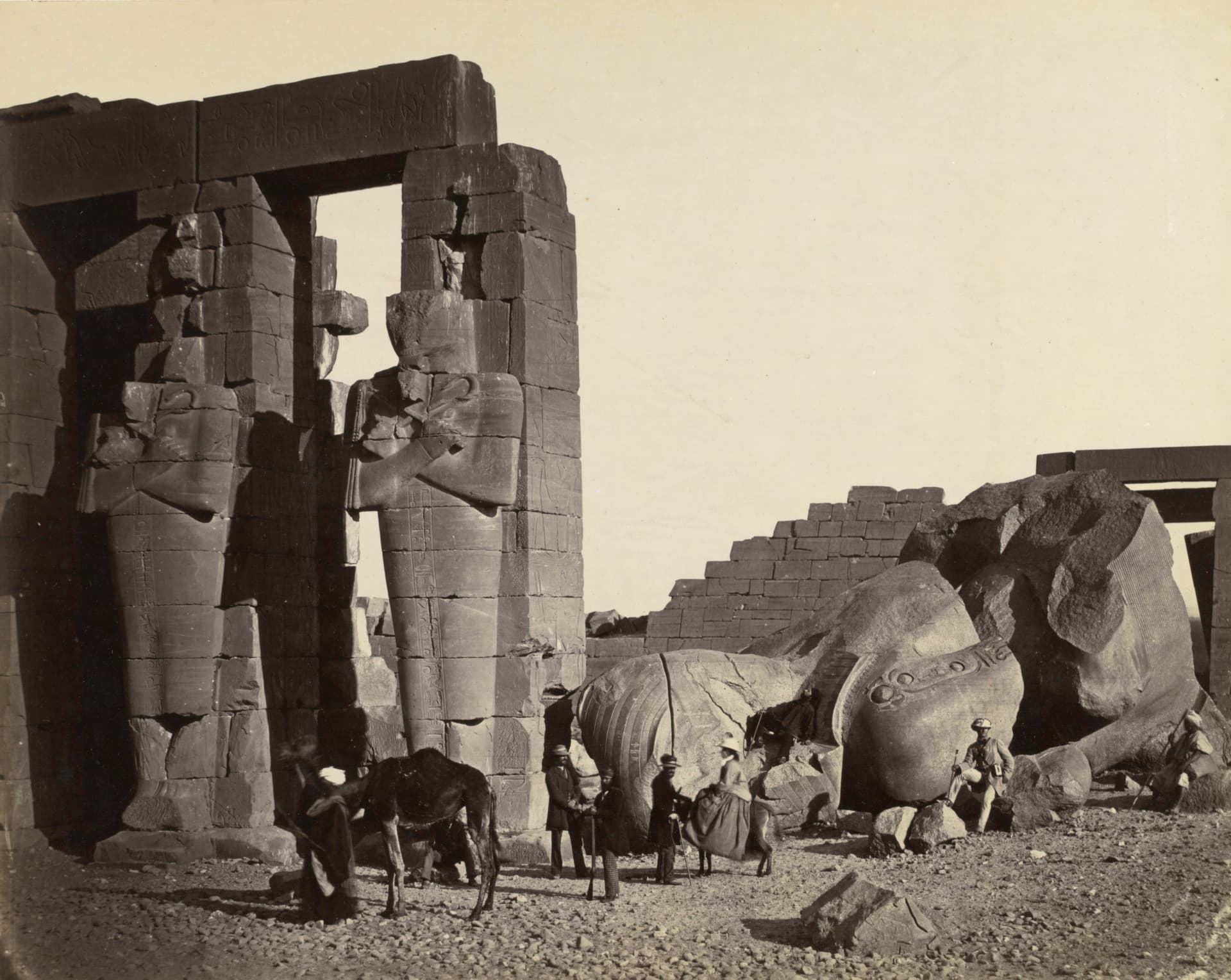A sepia photograph depicts a fallen statue at the ruin of the Ramesseum in Thebes.