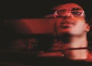 A blurred photograph depicts Stevie Wonder from the neck up, wearing glasses and looking up.