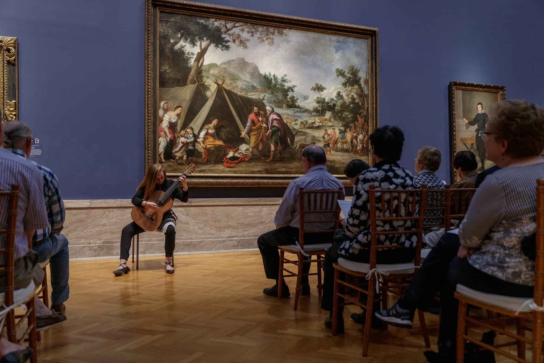 a group of people sitting in chairs watching a painting