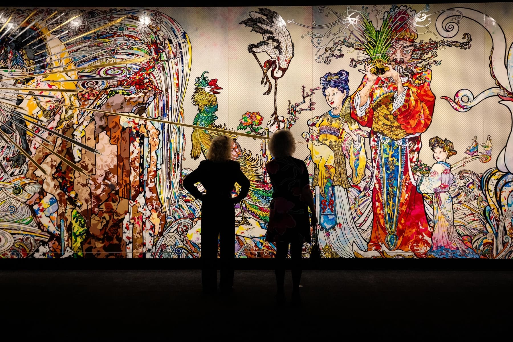 a couple of people looking at a painting on a wall