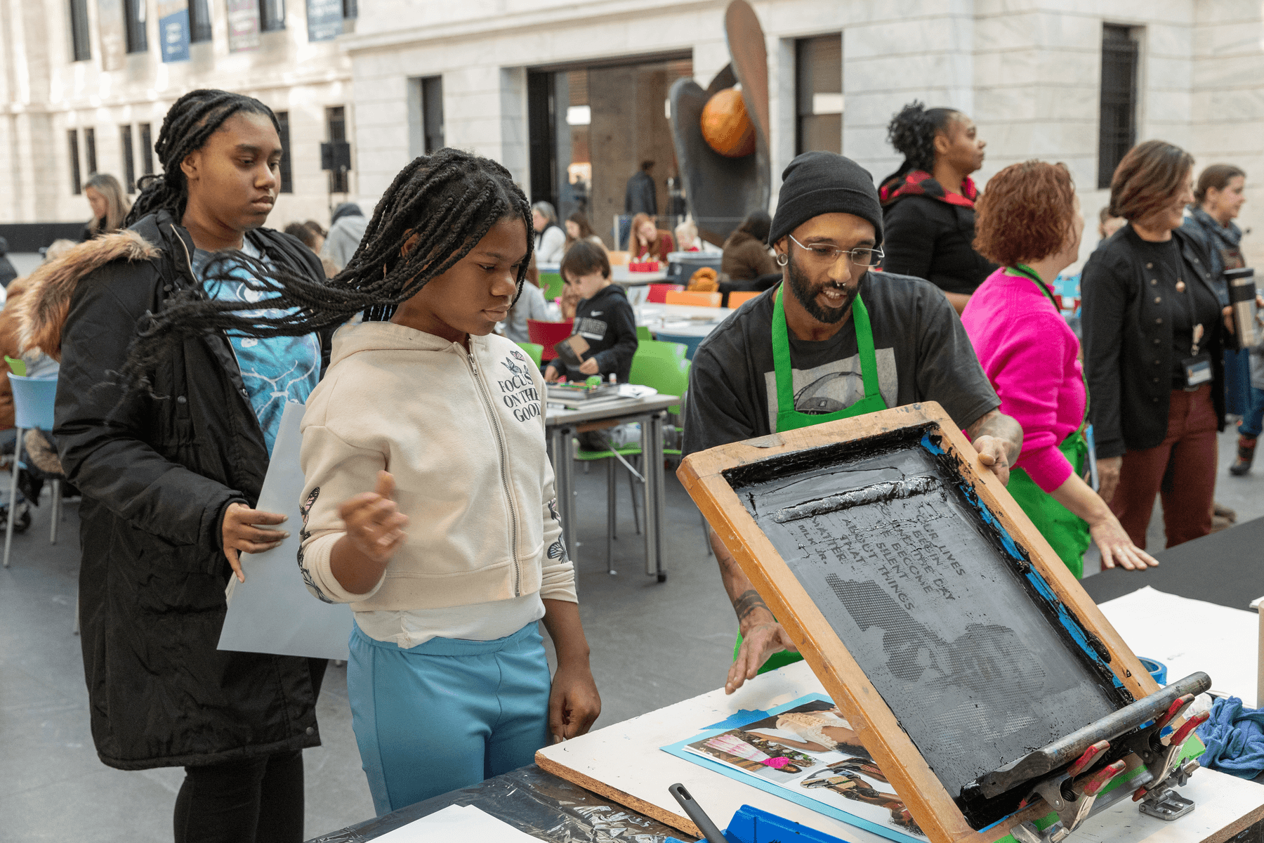 A young person screen printing a poster with the help of an art instructor.