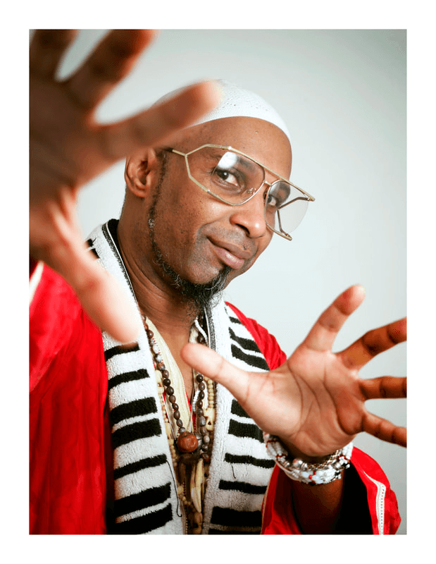 Omar Sosa wearing a white hat and glasses with his hand up