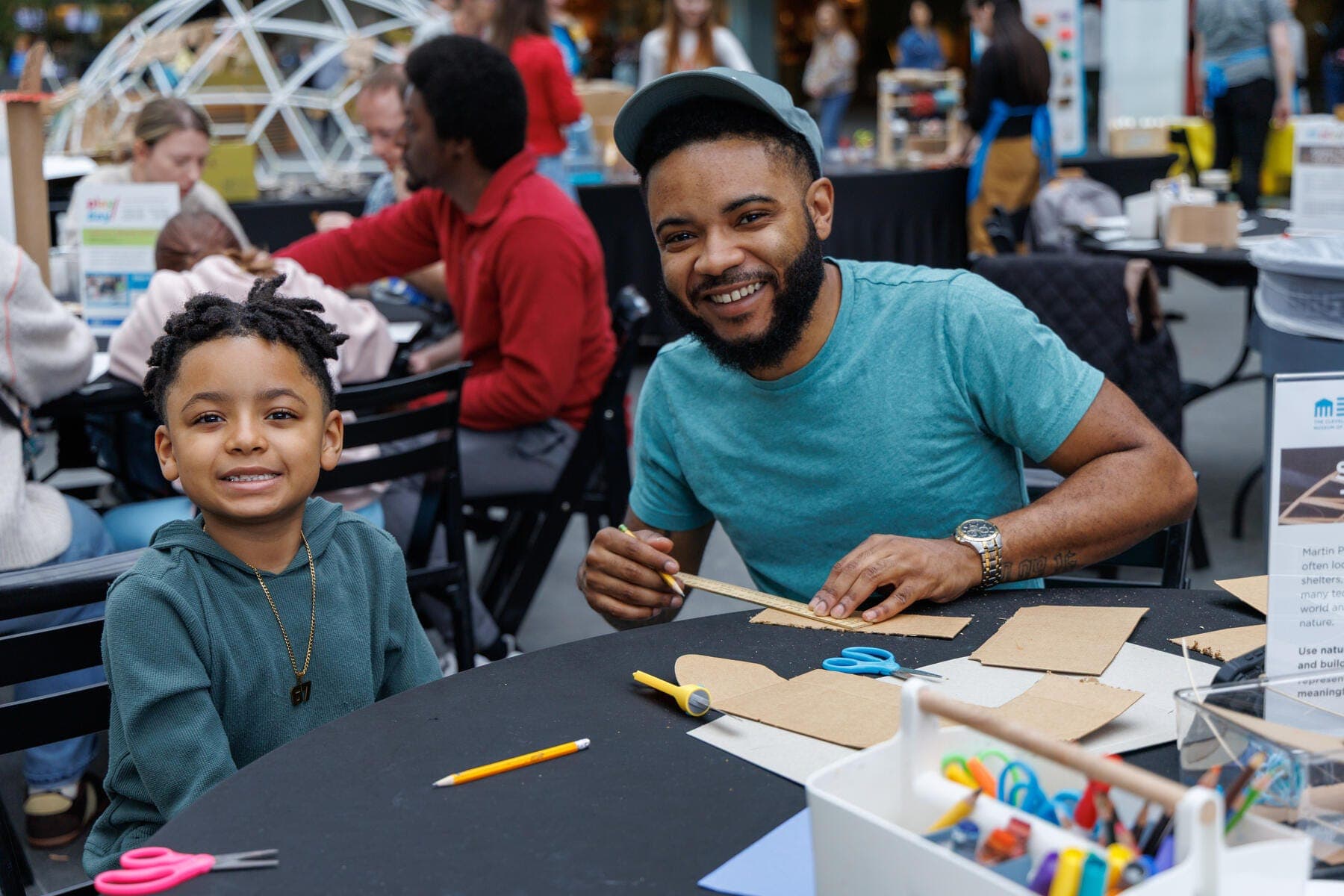 a person and a boy sitting at a table with pencils