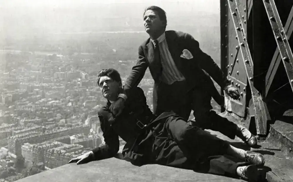 a man sitting on a ledge with a man standing on a roof