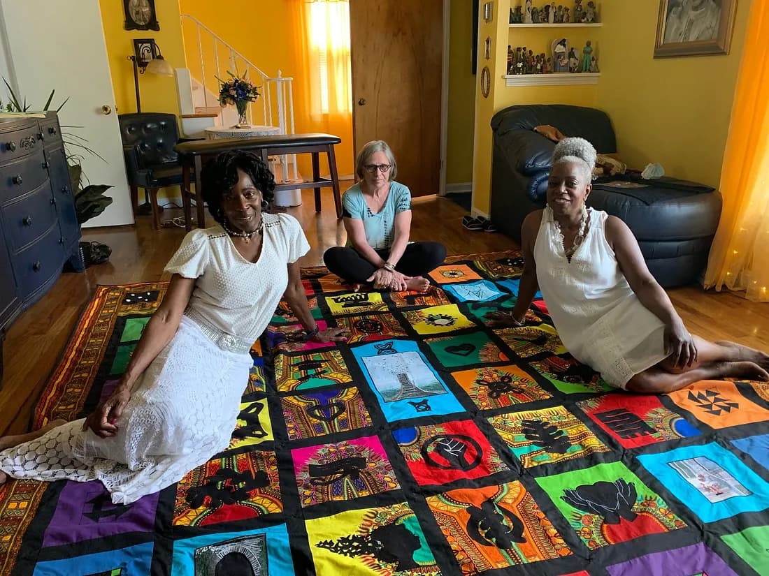 Three people sitting on top of a colorful quilt.