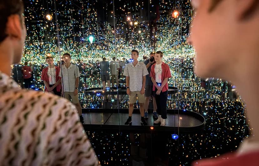Exhibition image of people in a dark room with speckled blue, green, and orange lights, reflected in mirrors.