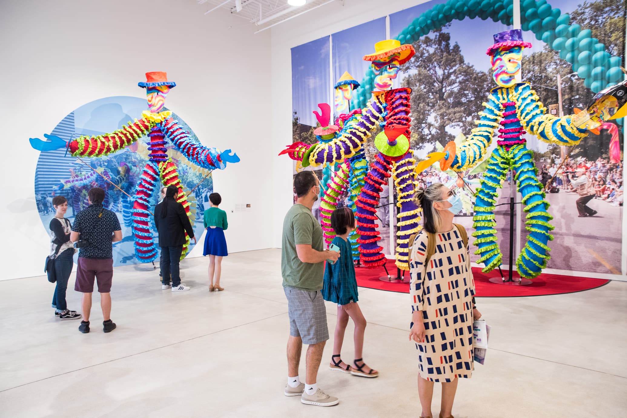 People view large, standing puppet figures in colorful gallery