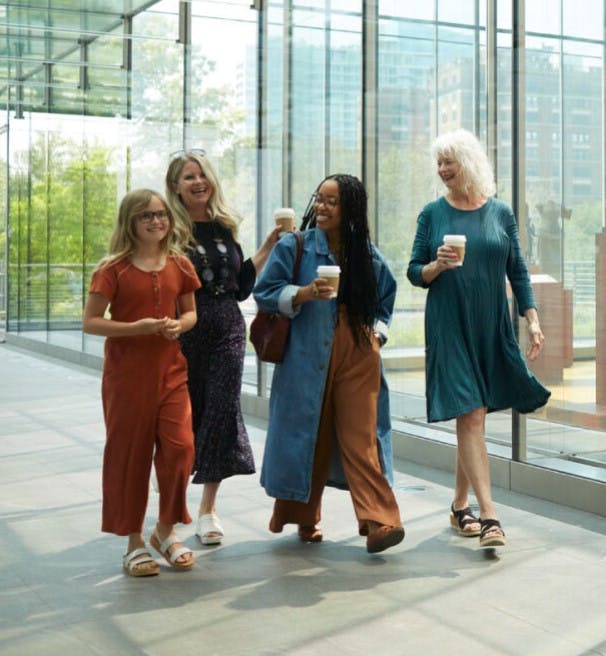 Four women walk through the glass hallway on the second floor of the museum