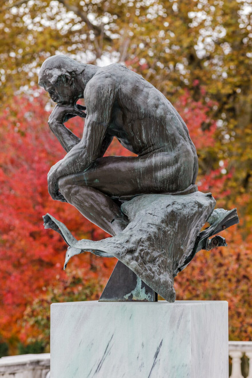 A side view of a statue outside of the CMA, with fall foliage behind it