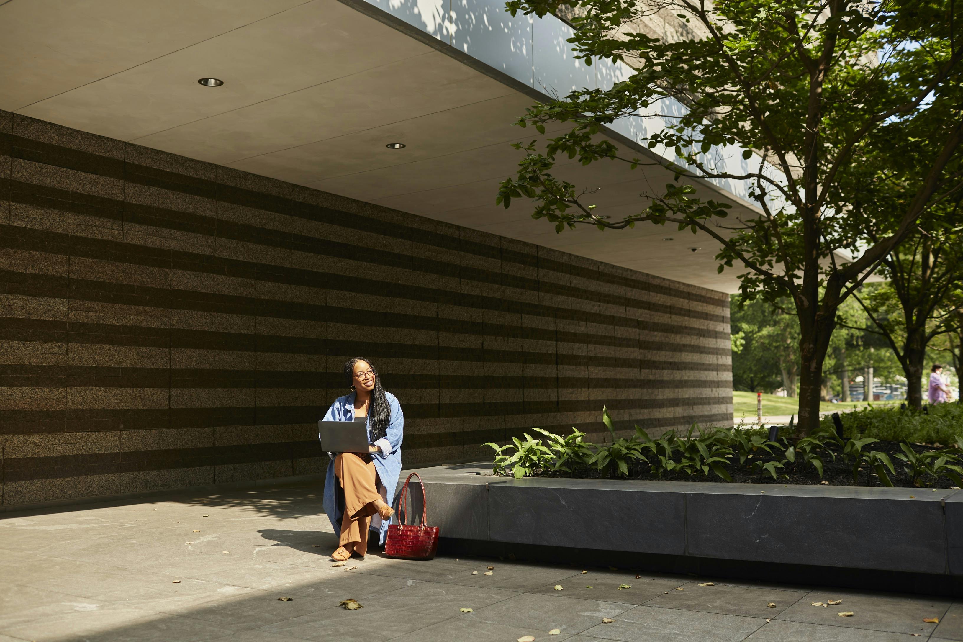 Woman sitting in the north court lobby, outside of the museum with a laptop