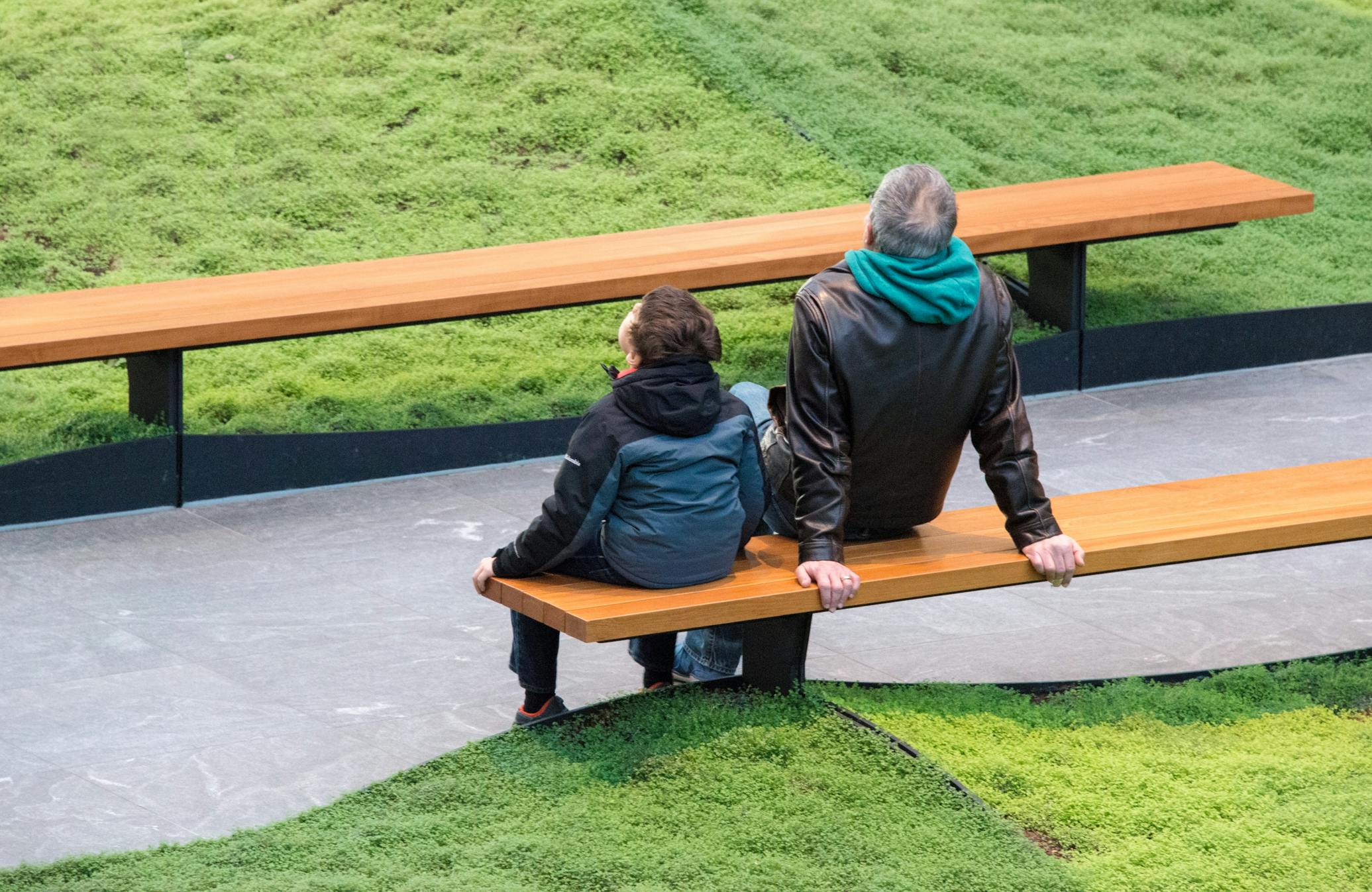 a man and a young boy sitting on a wooden bench in the atrium