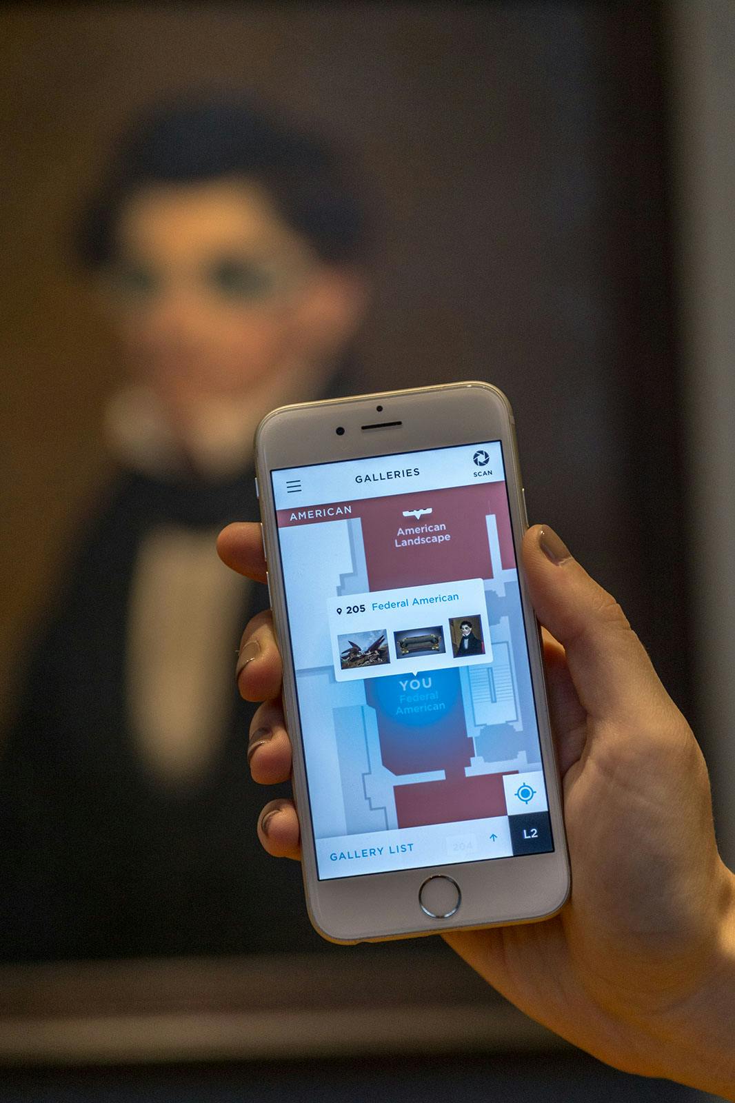A person holding a phone displaying the ArtLens App in front of a work of art