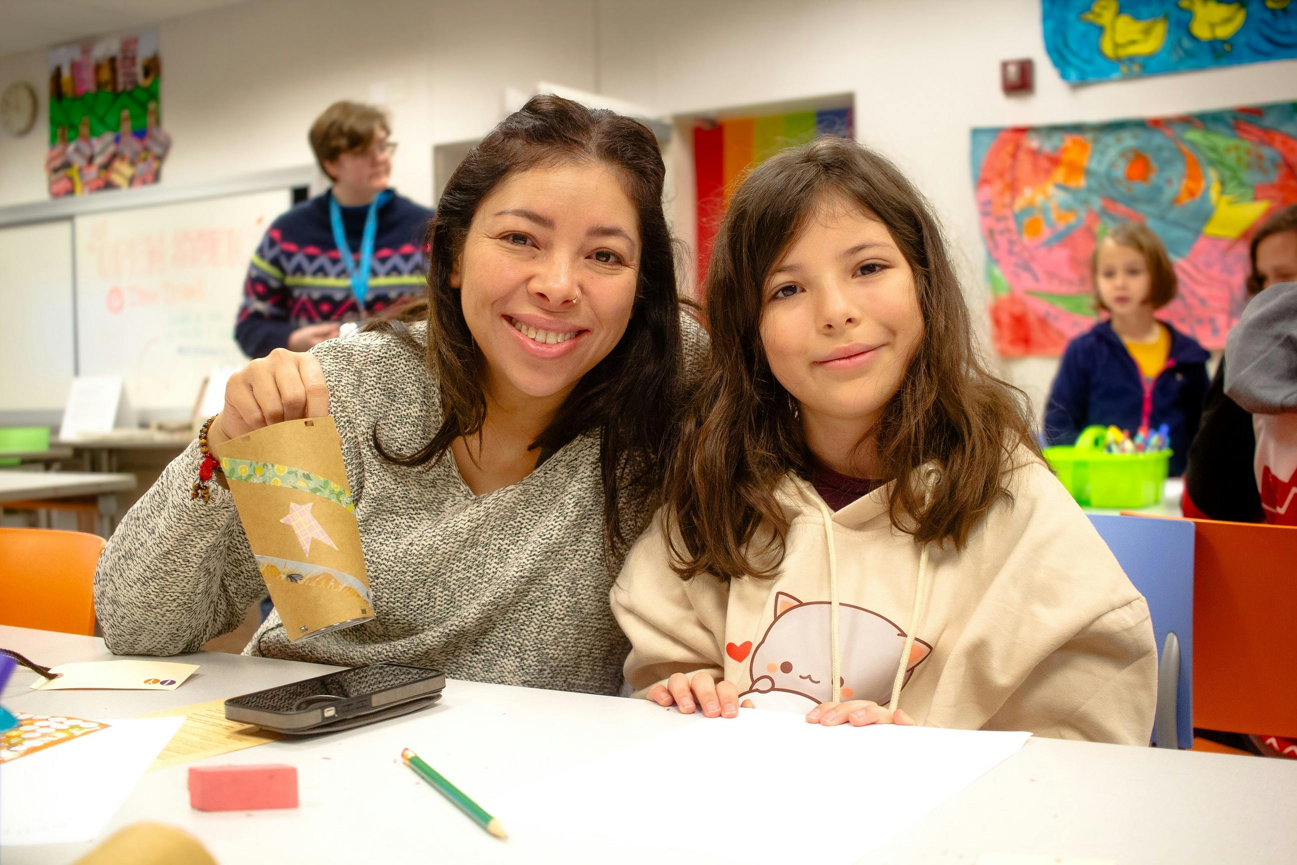 Woman and child sitting in art classroom holding up art project