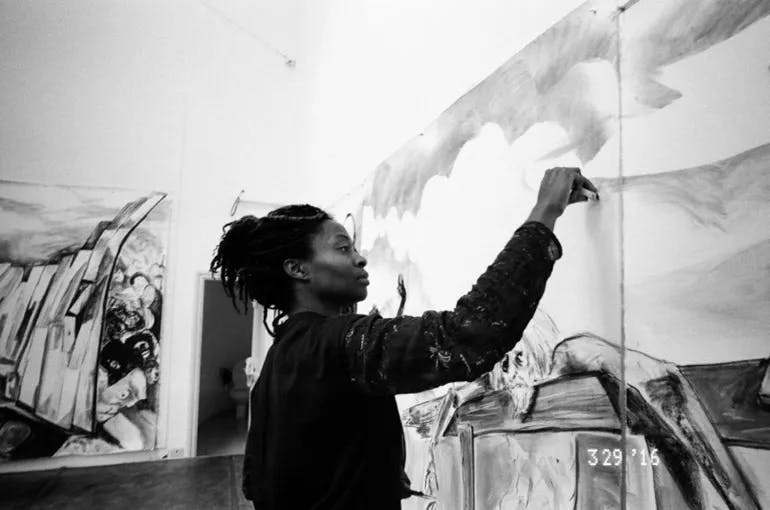 Black and white photo of the artist Kara Walker drawing on a large panel