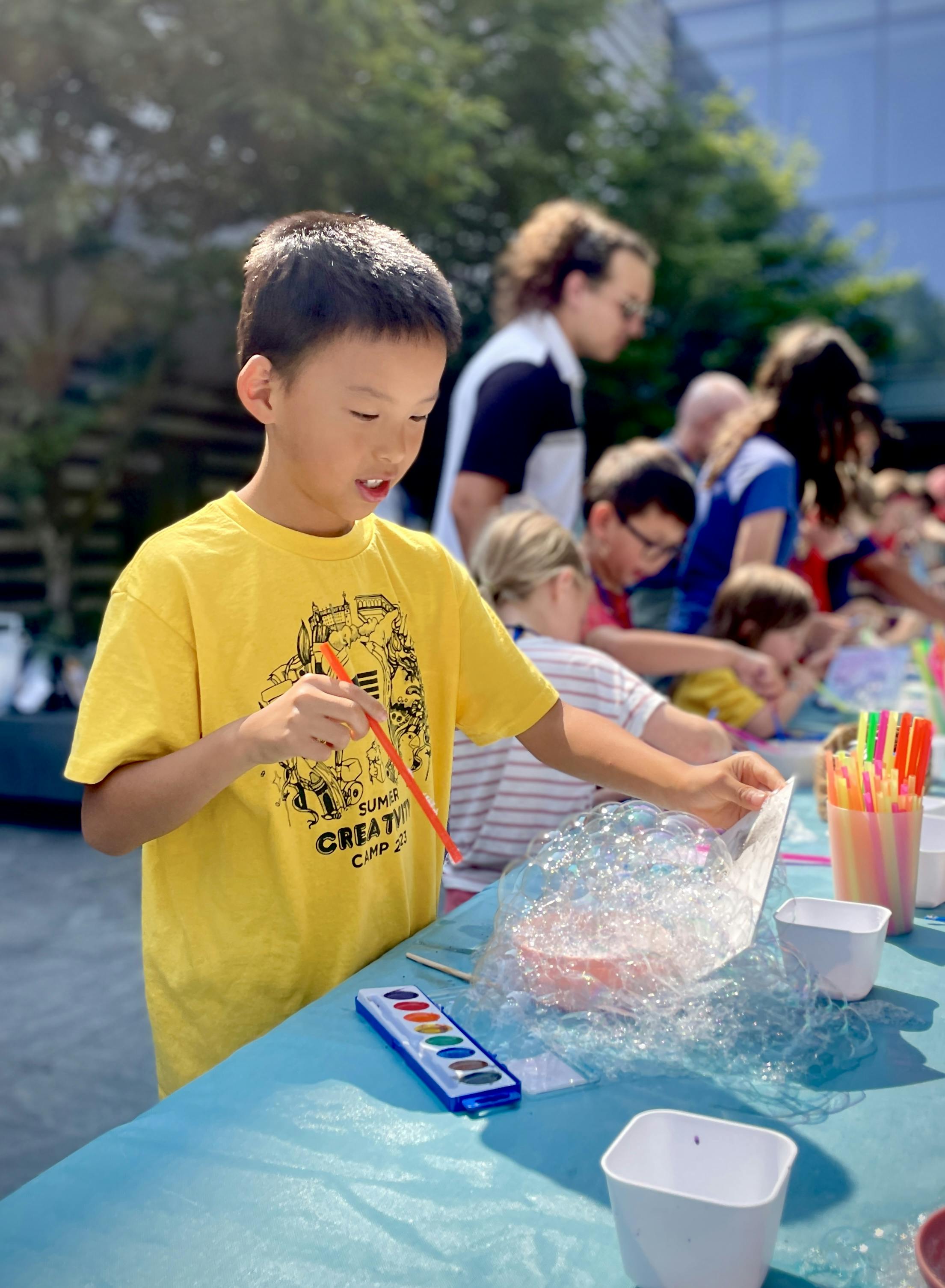 Child making bubble art painting project standing at a table outside