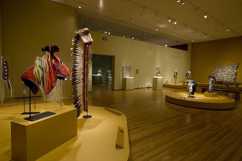 A large gallery with a red horsehead headress and a feather headress in the foreground