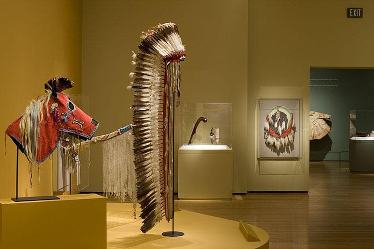 gallery view with a red horsehead headress and feather headress (that is the height of an adult)