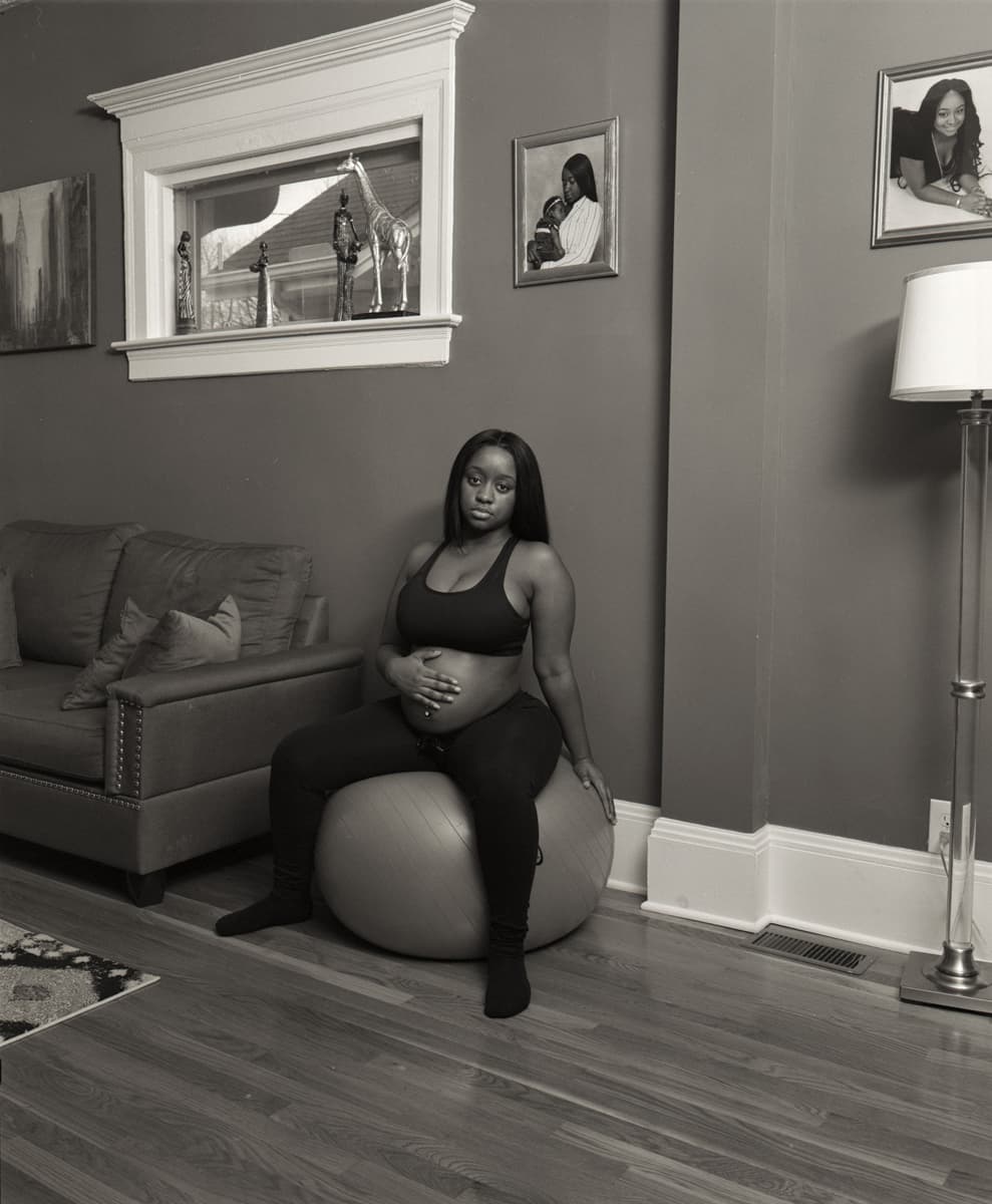 A pregnant woman sits on a birth ball in a living room.
