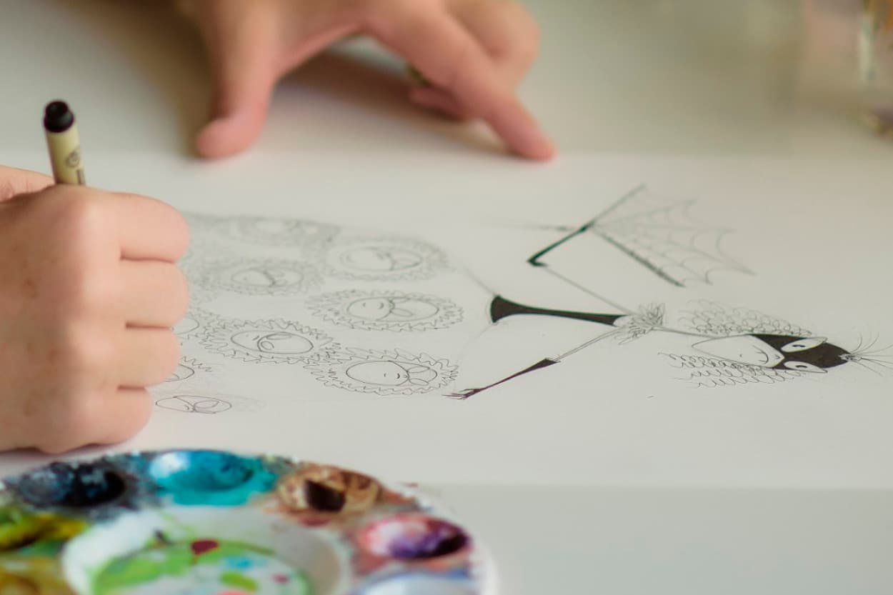 Artist hands drawing a black and white illustration of an stick-thin lady in a skirt with bug eyes.