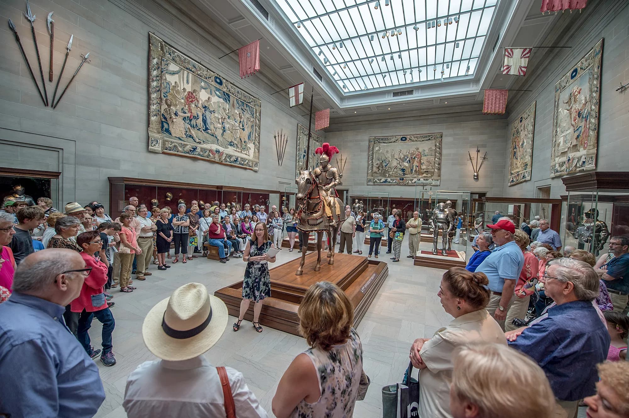 A suit of armor for a horse and rider displayed in the center of a gallery and around which visitors gather in a circle.