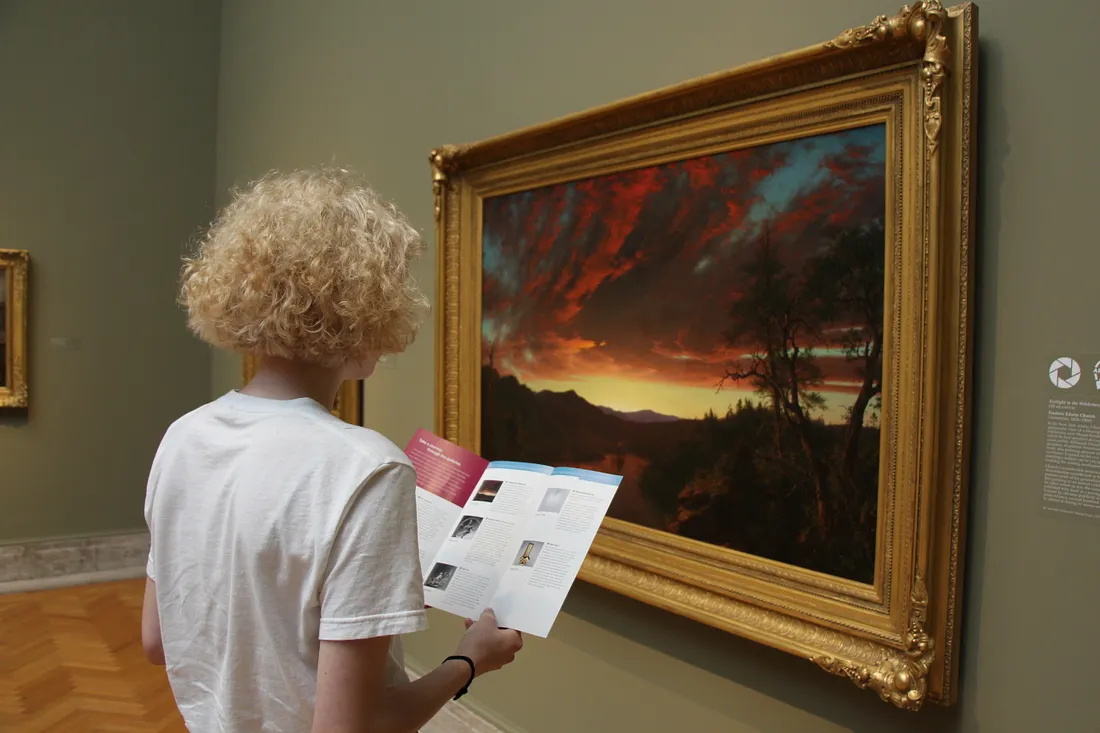 Visitor looking at a guide to the Kusama Connections tour in front of a painting.
