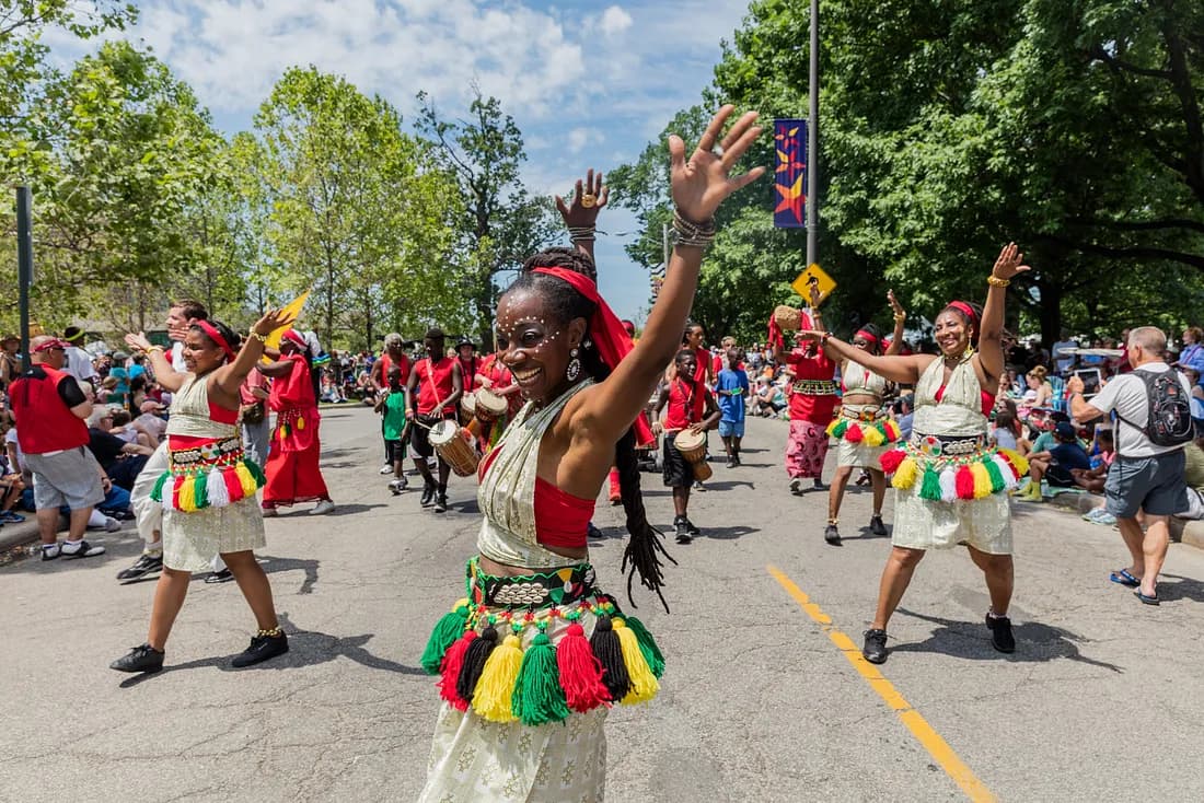 Many smiling people dancing down the street in colorful clothing in Parade the Circle.
