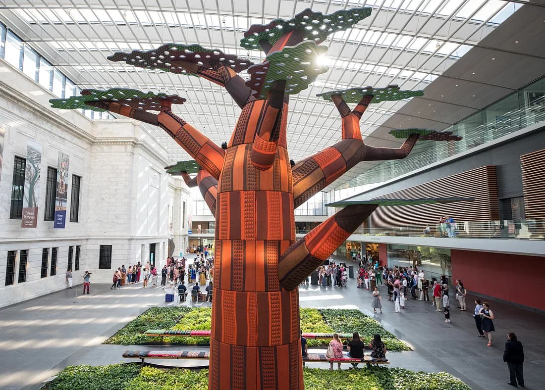 A stylized tree with a thick trunk and thick, stubby limbs branching out with hole-speckled, flat organic shapes like leaves on top. It is in the Cleveland Museum of Art's atrium.