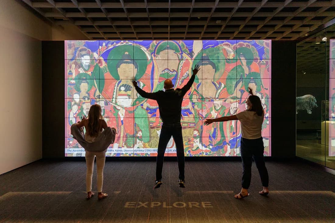 Three people waving their arms, using their movement to make an image become clear on the Zoom and Reveal Wall in ArtLens Studio.