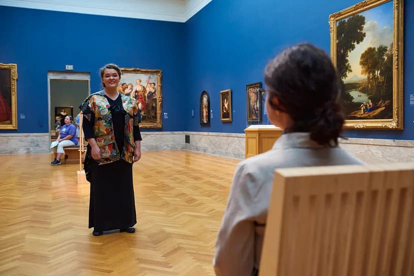 Person standing and singing surrounded by paintings in a gallery.