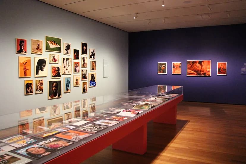 Installation image of The New Black Vanguard, featuring many colorful images hung on the walls and laid out in a glass case.
