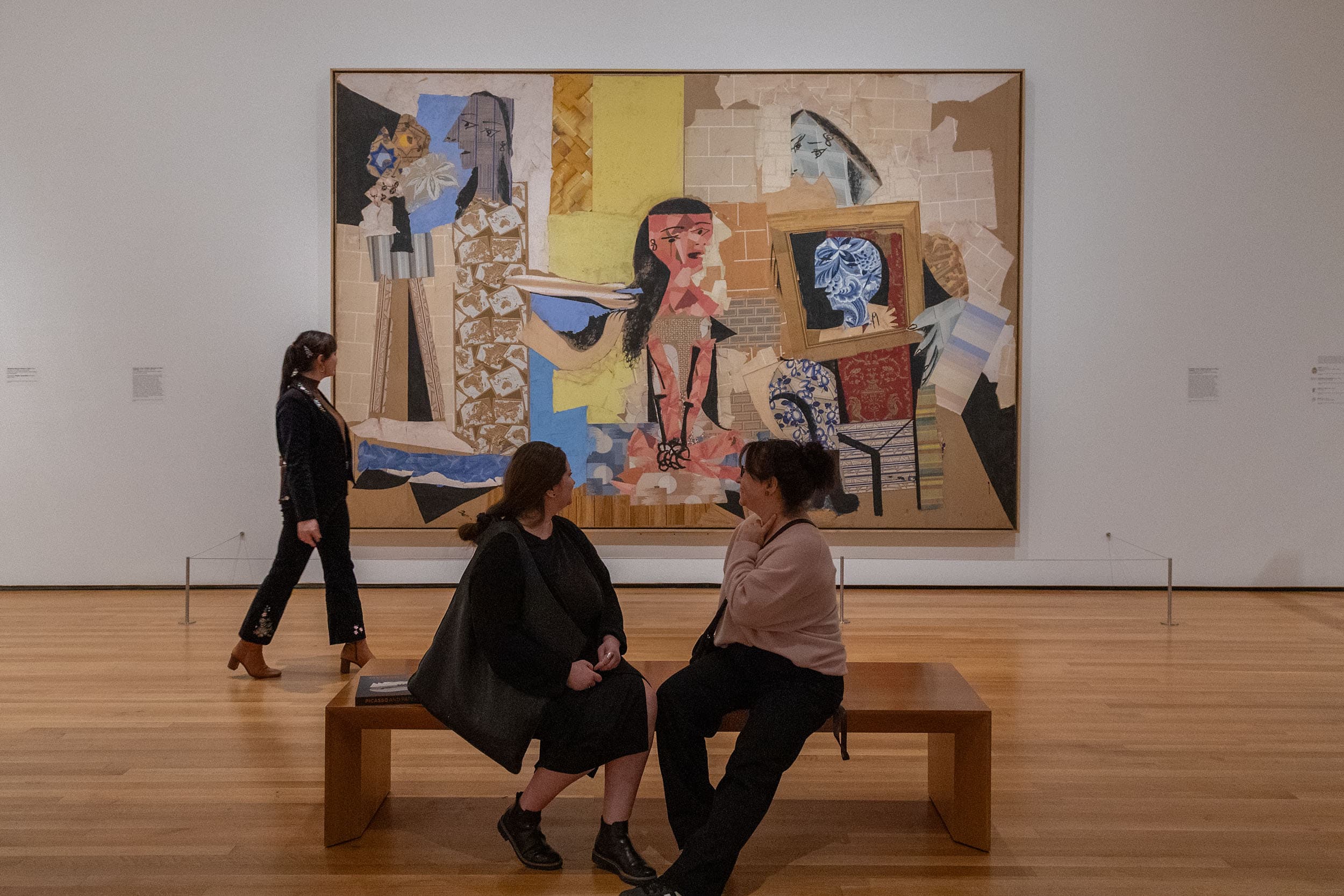 Gallery view of a large paper collage with 3 figures standing in front of it