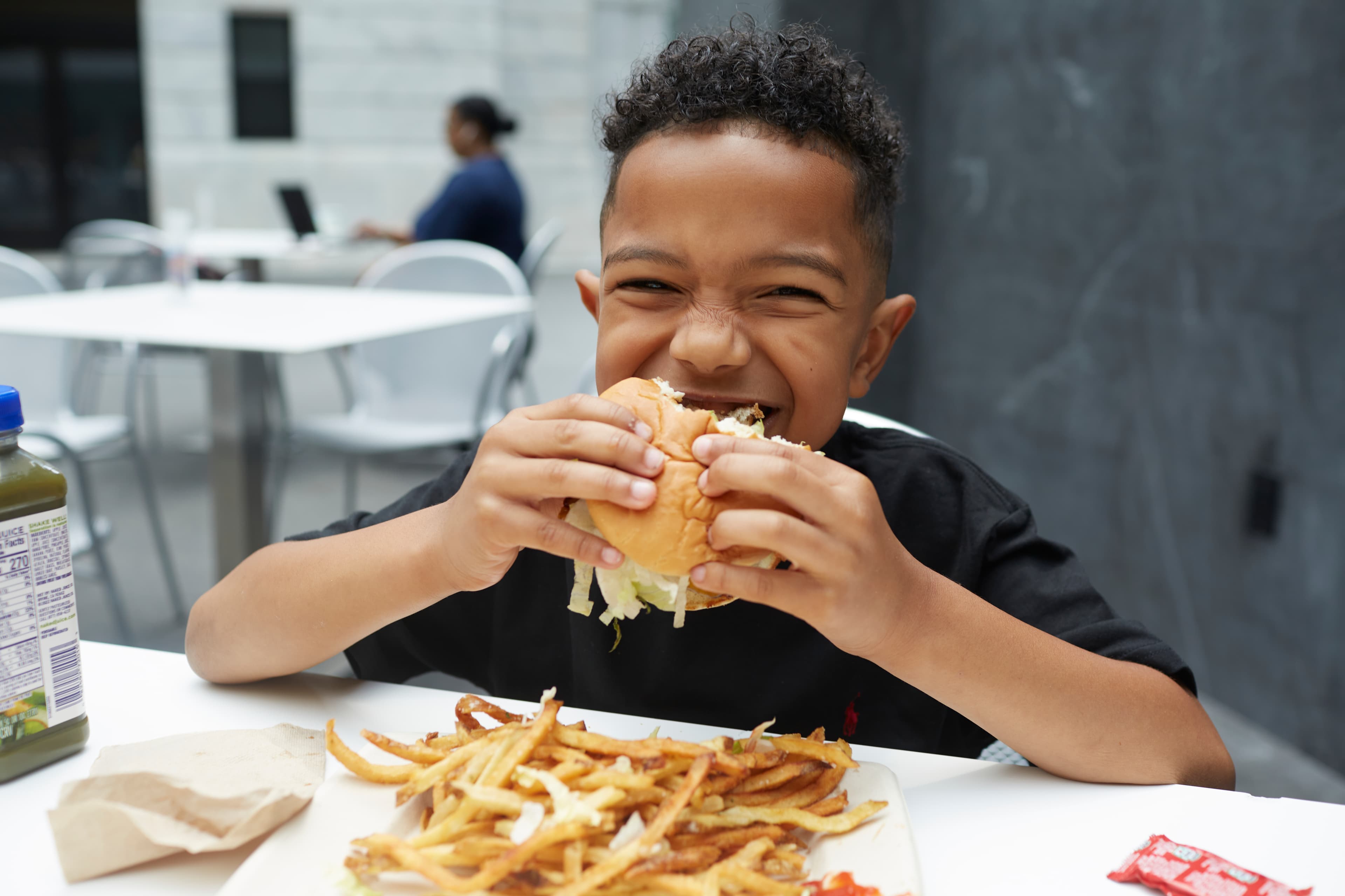 A young smiling boy is sitting at a table in CMA's atrium eating a burger