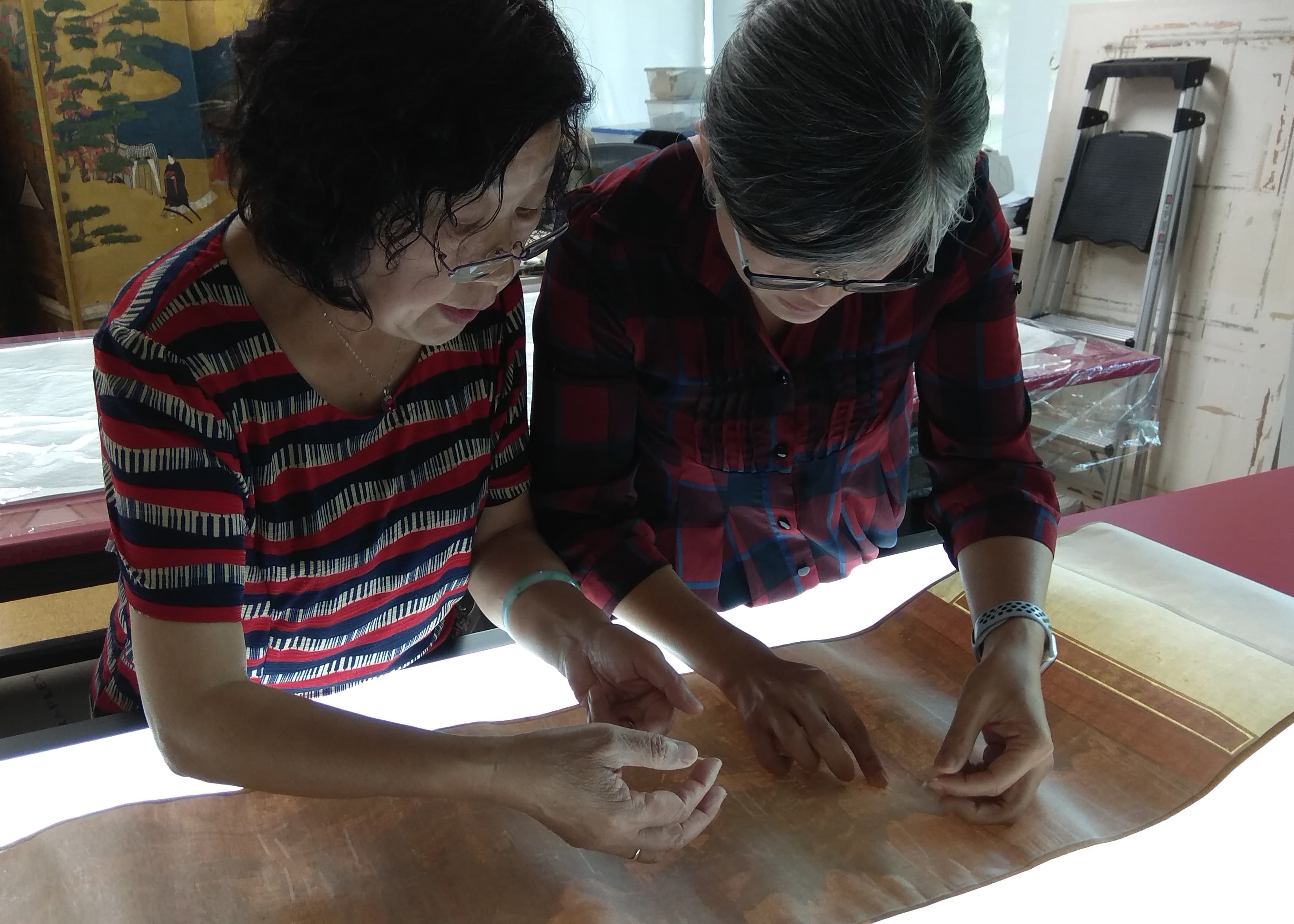 Pinfang Zhu, a skilled Chinese paintings conservator from the Shanghai Museum, China, demonstrates applying mending strips onto the damaged areas of a Chinese handscroll to Ika Hsiao, conservator of Asian paintings.