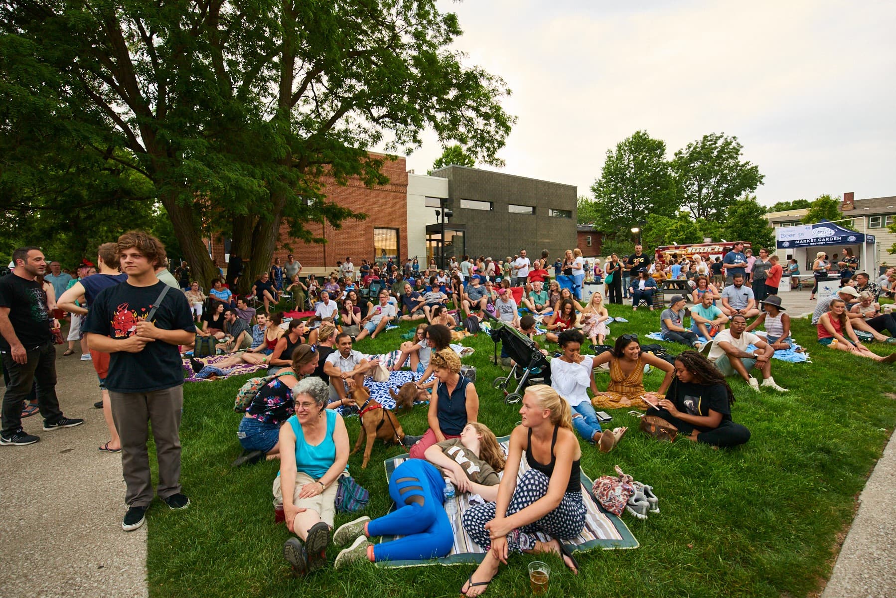 People sitting outside on blankets and chairs in front of a brick building