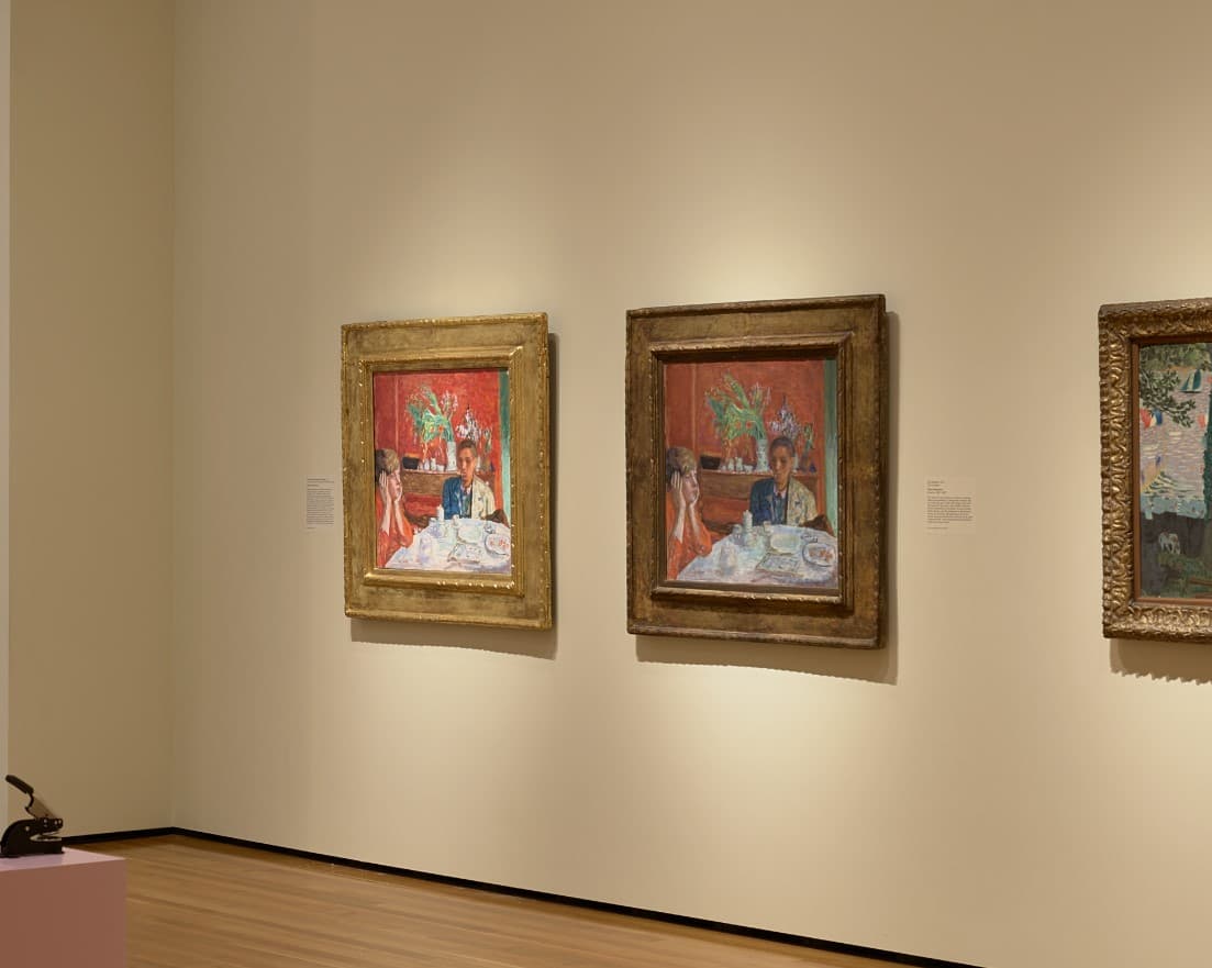 Two paintings on a wall next to each other, both identical, depicting two figures sharing a dessert at a dinner table