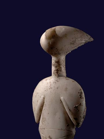 A small marble figurine bears vague features and tilts their head back, looking up. The head fans out slightly at the back and sports eyes and a nose on the face.