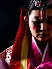 A woman in marriage attire and shown from the shoulders up looks down.