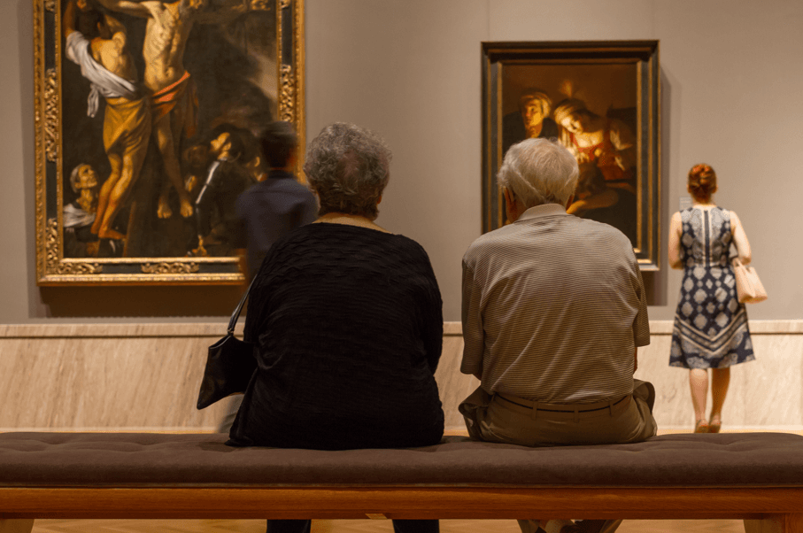 two individuals sitting on a bench observing art while seated on a bench.