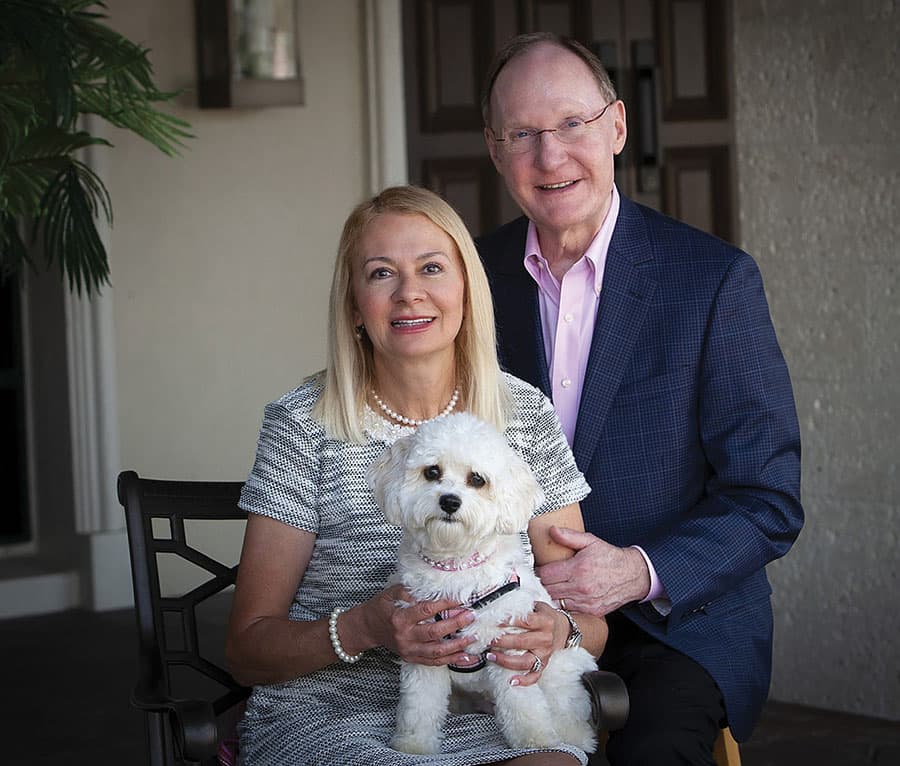 A portrait of a couple with their white dog in their home.
