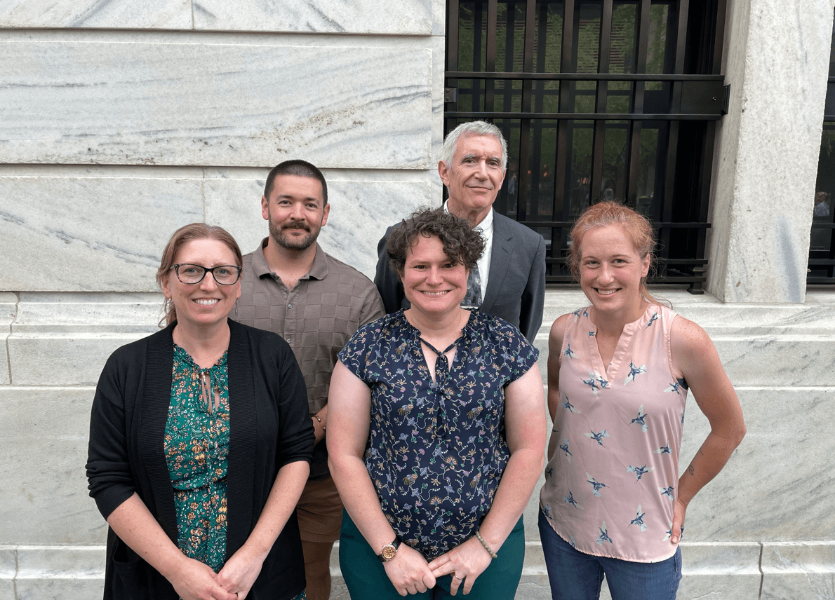 Five people standing against a marble wall smiling