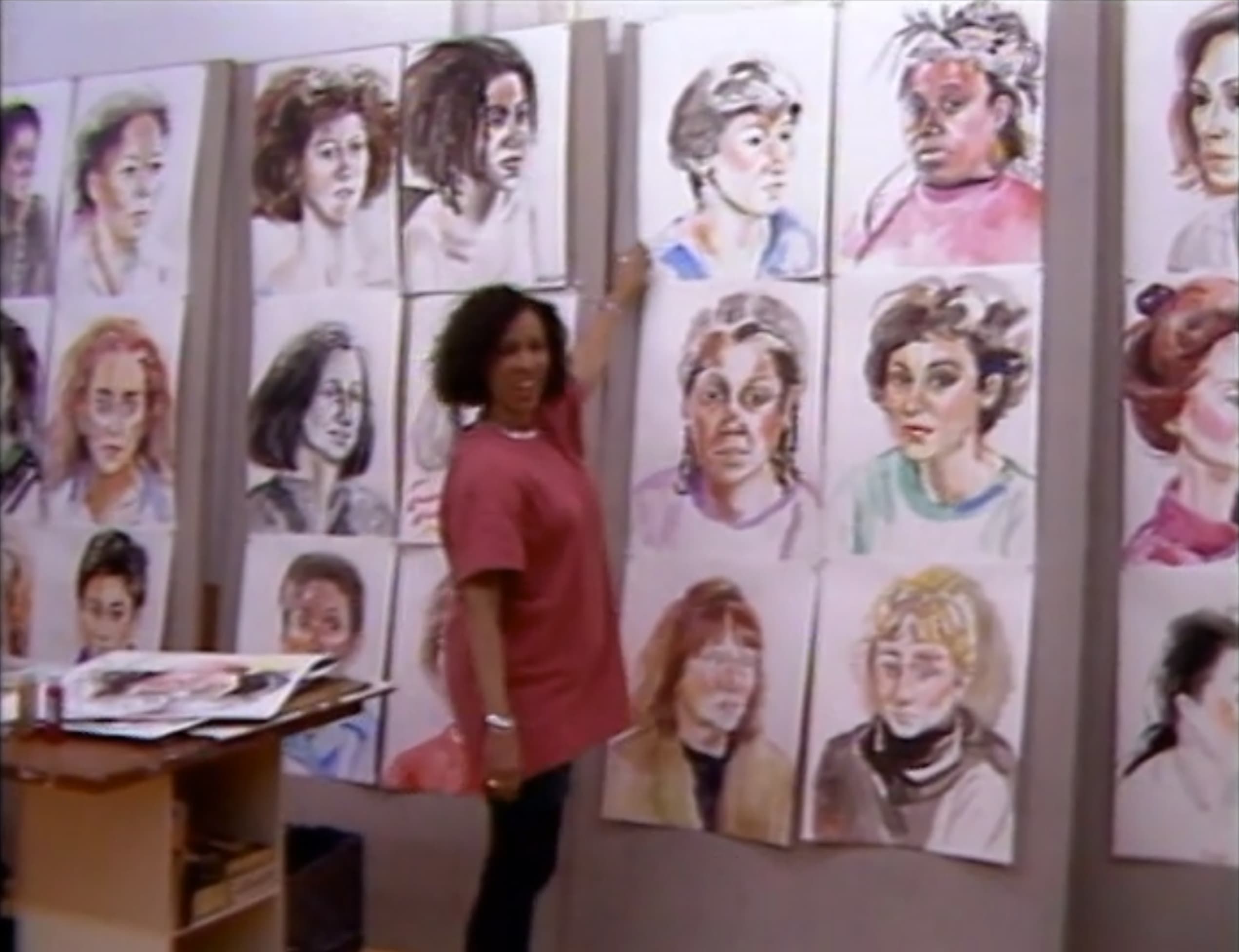 Emma Amos points at watercolor portraits from "The Gift" in her studio.